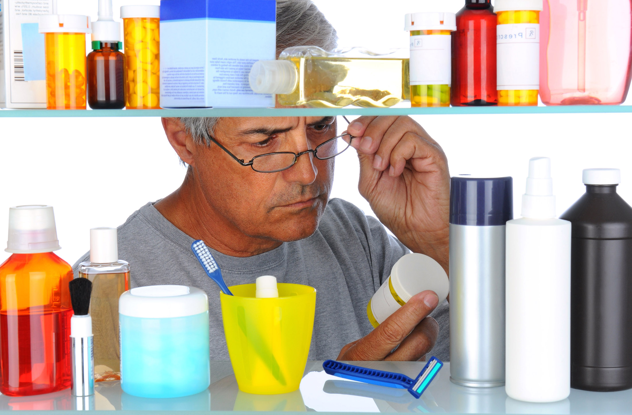 Unshaven Middle aged man reading a prescription label in front of his bathroom Medicine Cabinet.